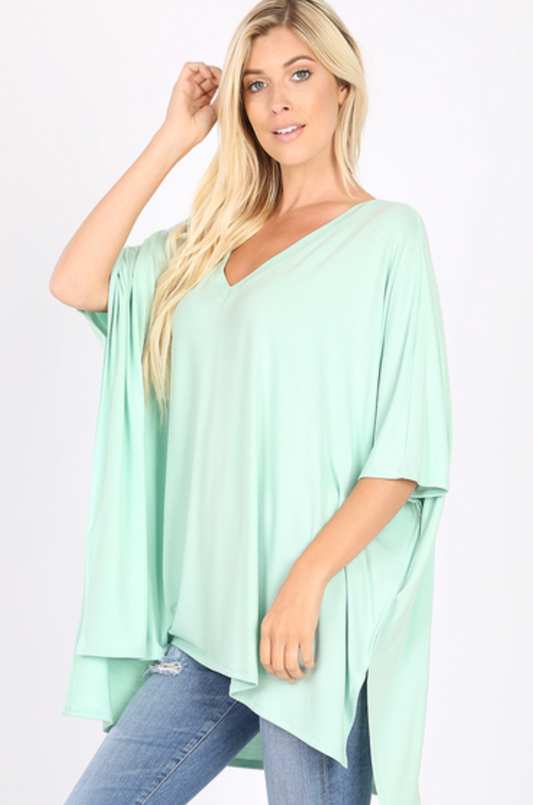 Model standing half cocked with right leg bent. Modeling dusty mint colored oversized poncho. Wearing skinny jeans.