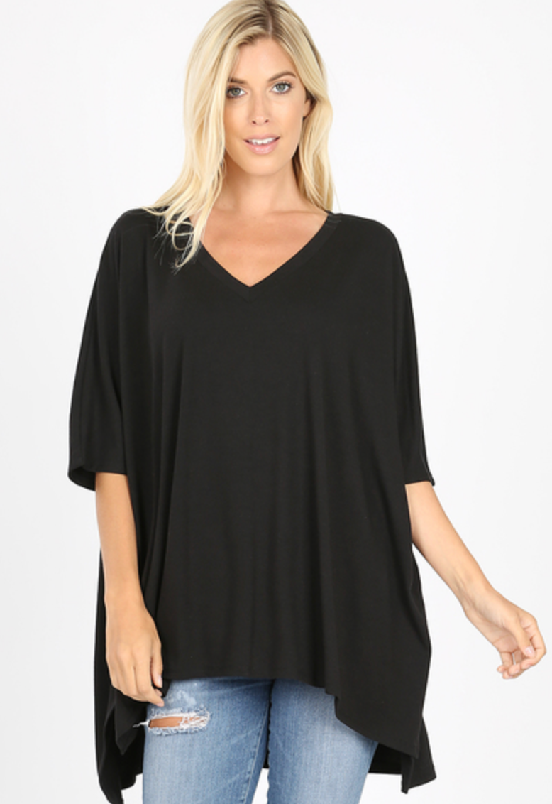 Black V-neck poncho top. Model is facing forward with left arm outstretched. Model is wearing jeans with hole on right thigh.